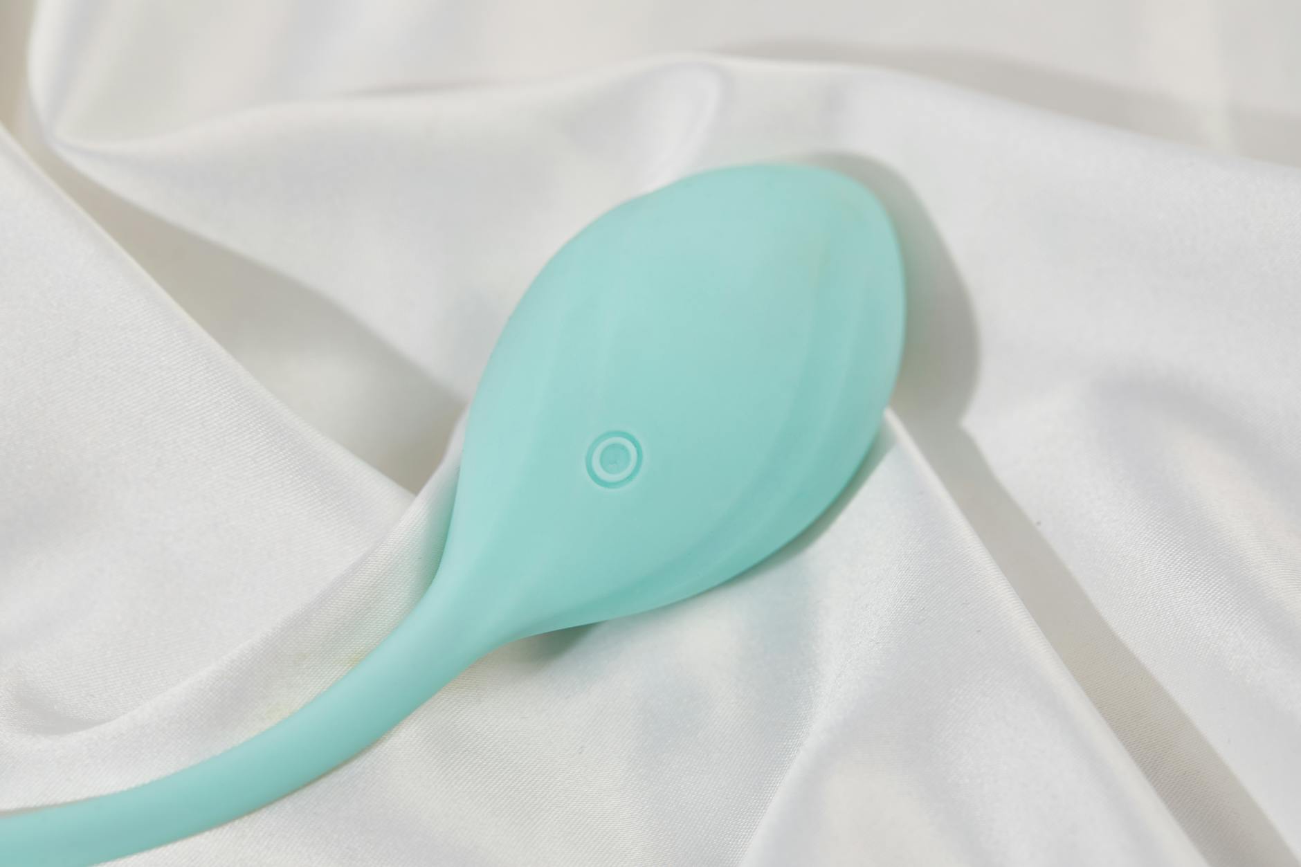 A sleek teal clitoral suction vibrator on smooth white silk fabric