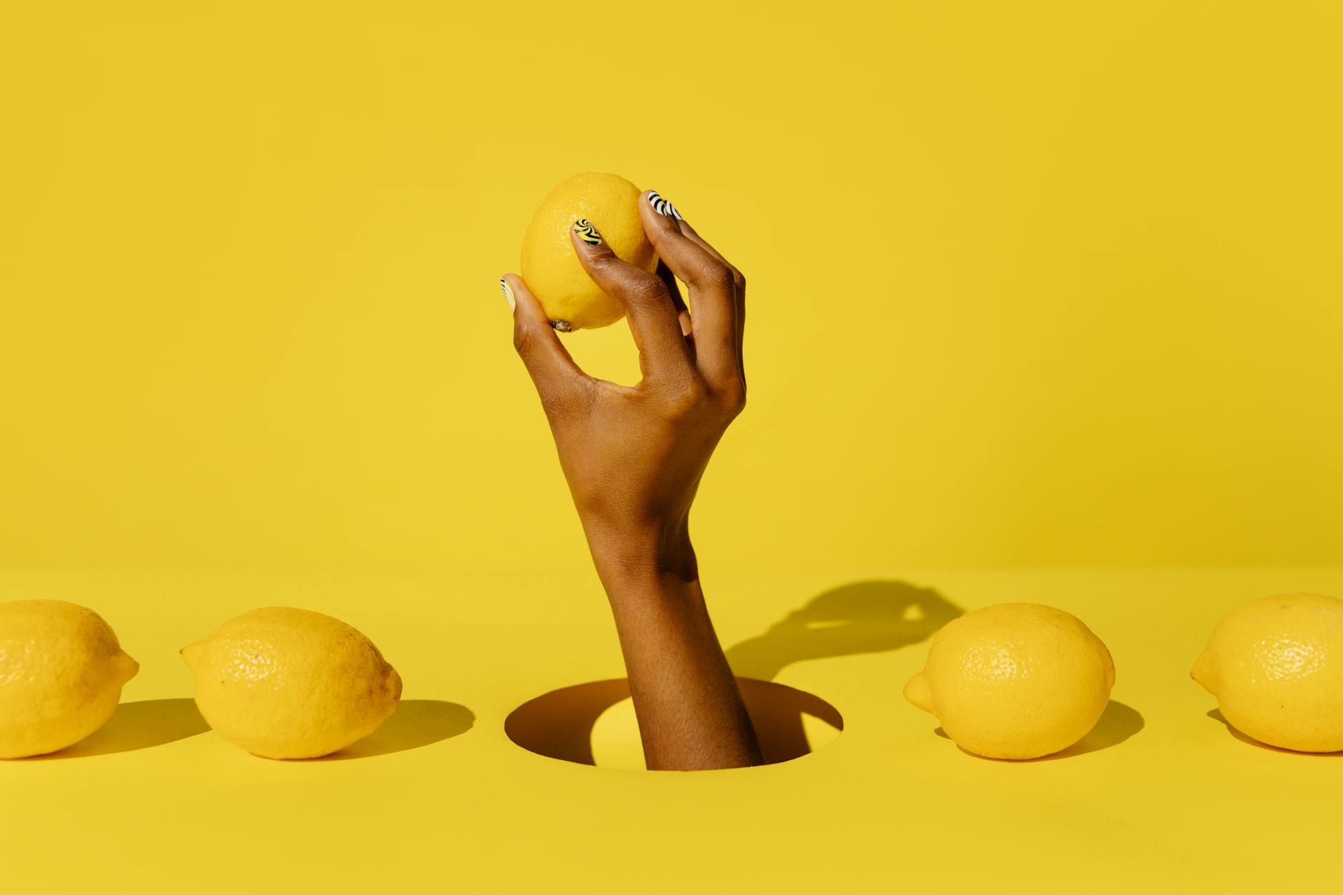 A hand holding a fresh lemon against a vivid yellow background, symbolizing renewed sensation and vitality