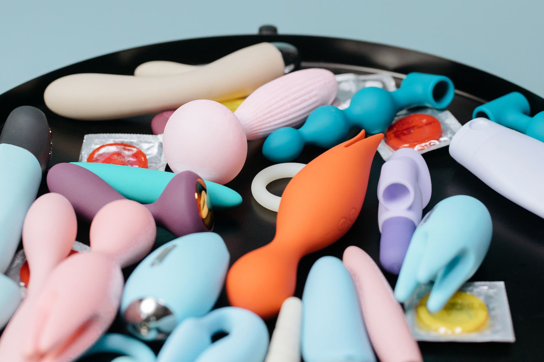 A vibrant collection of various clitoral vibrators and toys on a black tray, featuring diverse shapes and colors.