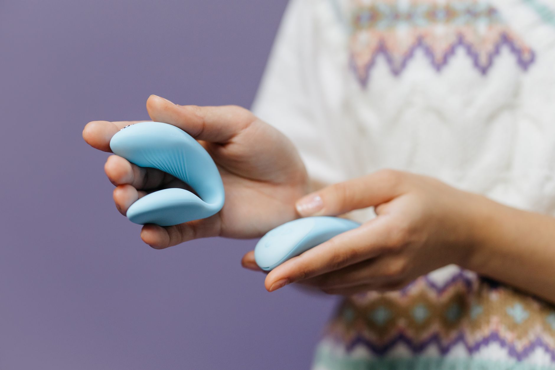 A hand holding a sleek blue vibrator against a purple background