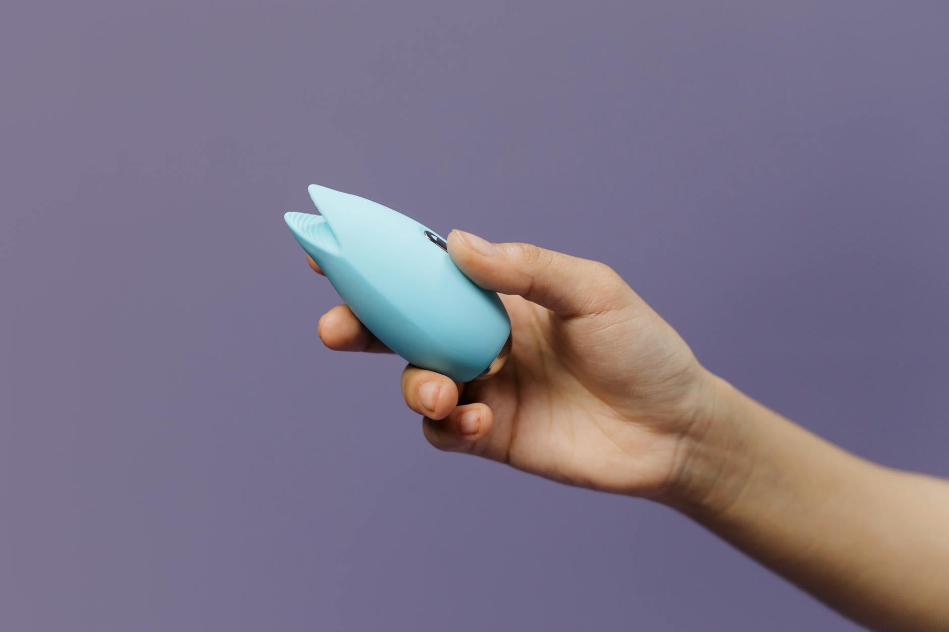 Mulher segurando vibrador azul e rosa em postura contemplativa contra fundo pastel